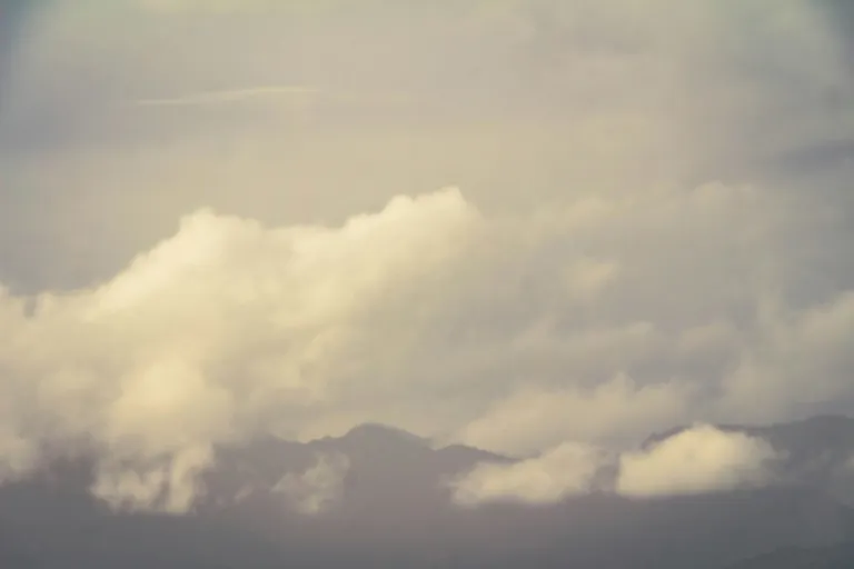 a plane flying through a cloudy sky with mountains in the background