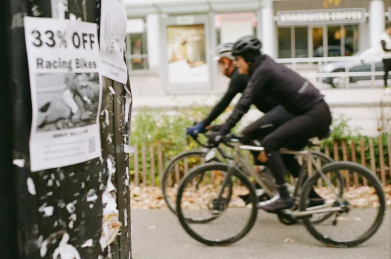Two cyclists ride past a poster advertising racing bikes.